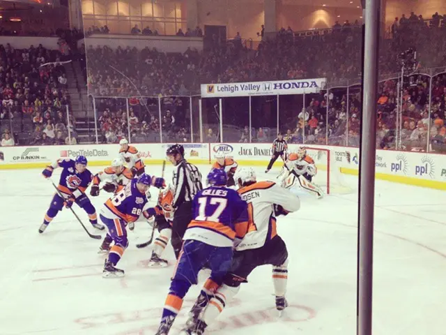 This image is taken in a stadium. At the bottom of the image there is a board and a pole. In the...